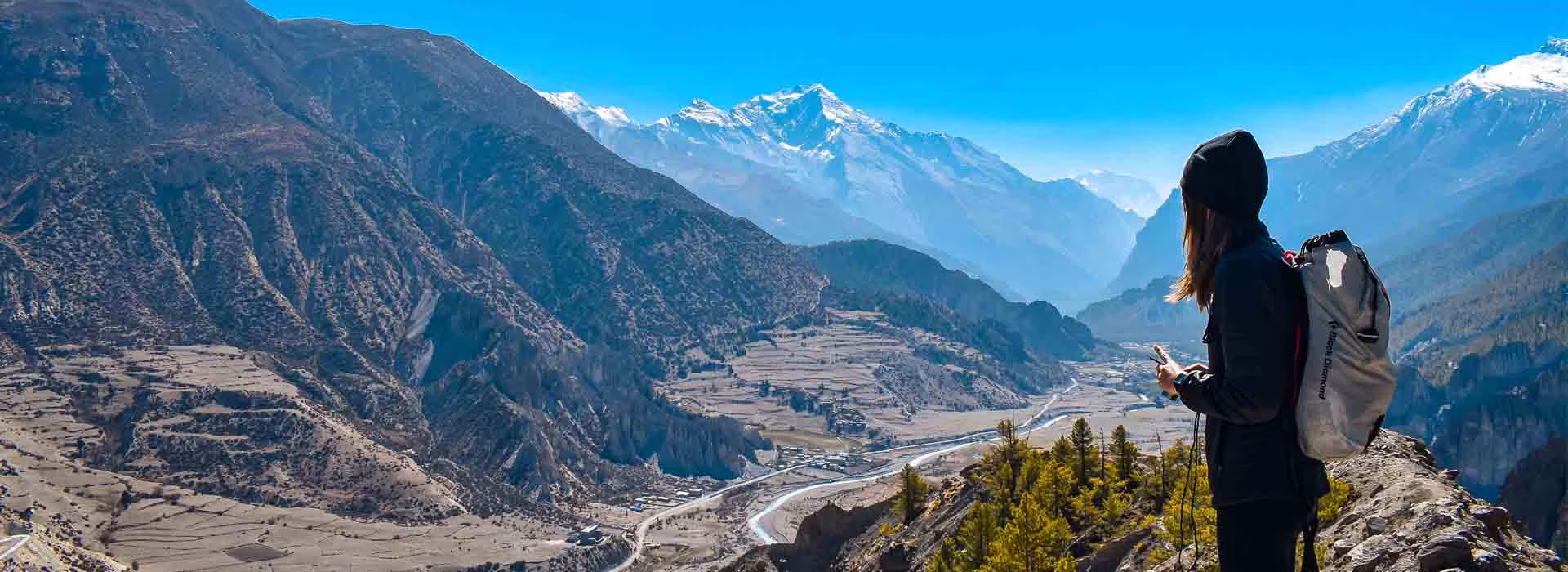 Female trekker standing in the Nepal Himalayas with mountains, river, and green hills