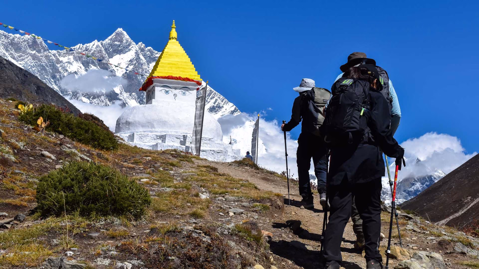 Three trekkers walking past a Buddhist stupa on the Luxury Everest Base Camp Trek with Himalayan views.